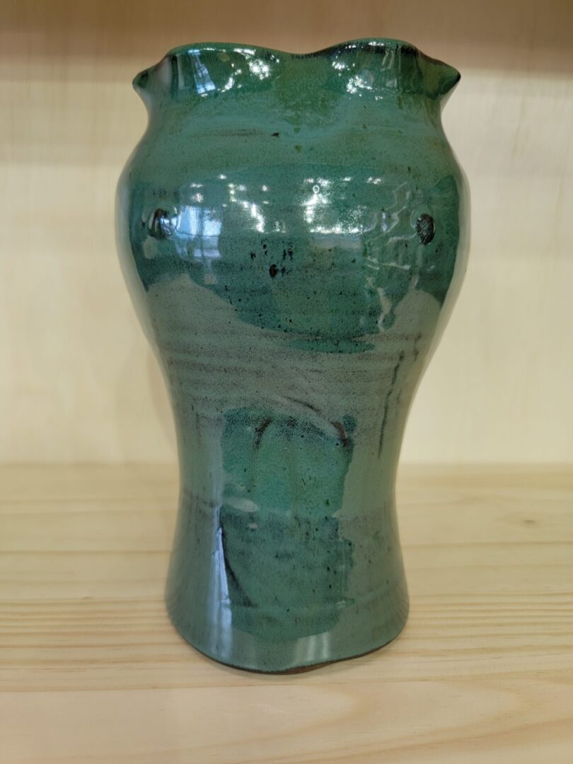 A green vase sitting on top of a wooden table.