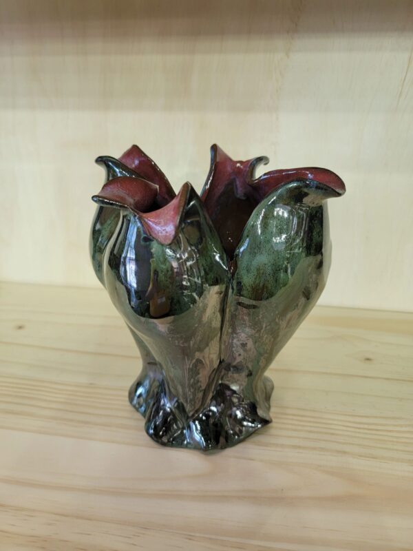 A green vase with two flowers on top of a wooden table.