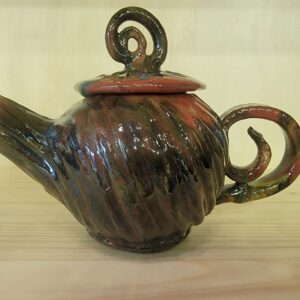 A brown teapot with red swirl design on top of wooden table.