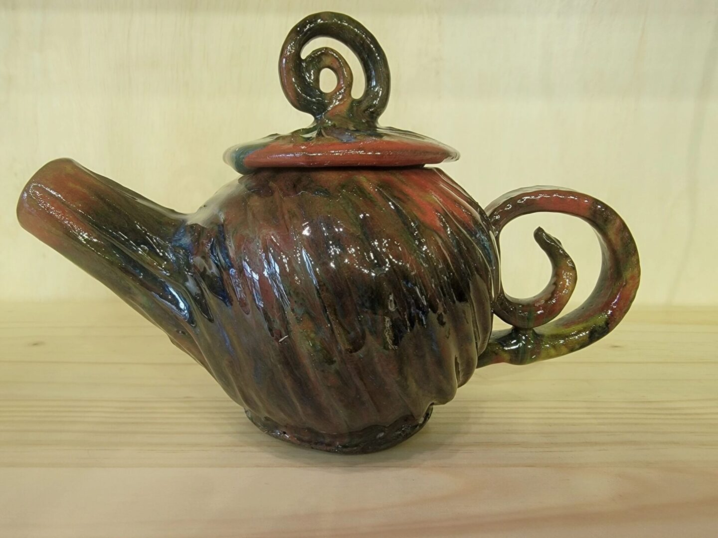 A brown teapot with red swirl design on top of wooden table.