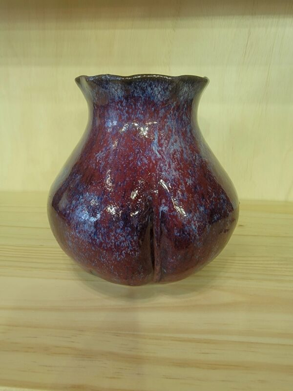 A red vase sitting on top of a wooden table.