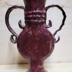 A red vase with two handles on top of it.