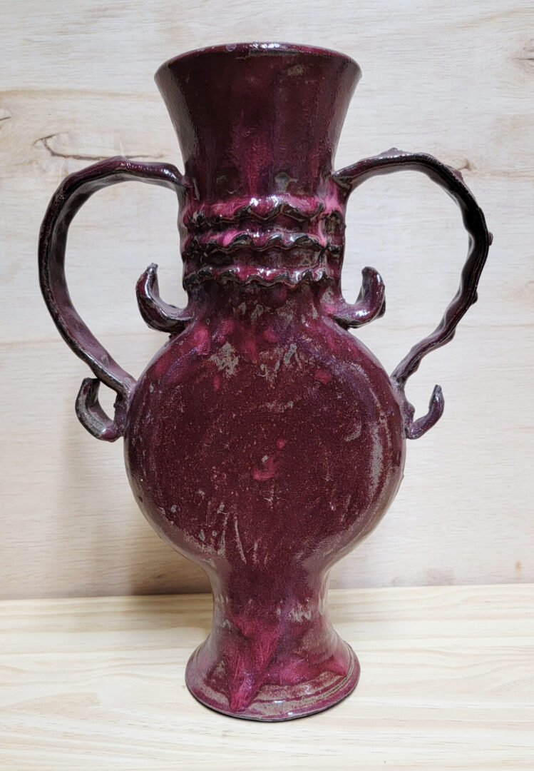 A red vase with two handles on top of it.