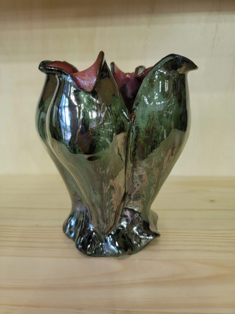 A green vase with red inside is sitting on the table.
