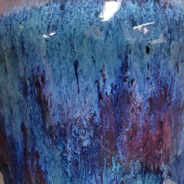 A blue vase with purple and red paint on it.